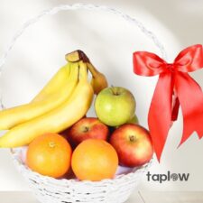 White wicker fruit basket with bananas, apples and oranges tied with a red ribbon.