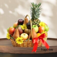 Wicker fruit basket featuring pineapple, pears, apples and decorative yellow flowers with ribbon.