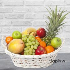 White wicker basket filled with grapes, mango, apples, oranges and a pineapple.