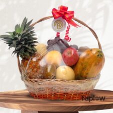 Decorative fruit basket with pineapple, apples, bananas and grapes on a wooden surface.
