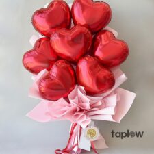 Cluster of red heart-shaped foil balloons in pink paper wrap