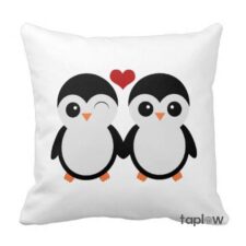 White cushion with two cartoon penguins holding a small heart