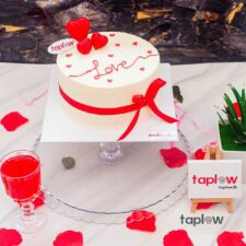 Round white 'Love' cake with red ribbon and heart toppers on table (product image).