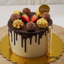 Round chocolate cake topped with truffles, strawberries and decorative wafer sticks.