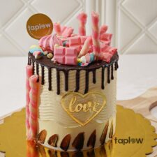 Cream drip cake decorated with pink candy swirls, marshmallow twists and a gold 'love' topper.