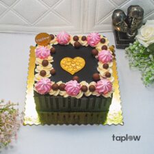 Square chocolate cake with black top, pink buttercream rosettes and a gold heart centre.