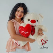 Woman holding white teddy bear with red heart cushion