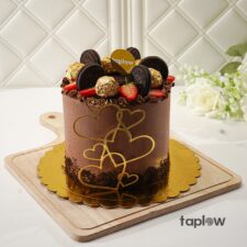 Close-up of chocolate cake decorated with Oreo cookies, strawberries and a gold heart frosting detail.