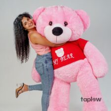 Large pink life-size teddy bear with red shirt a young wowen holding this